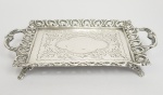 DELICADO TABULEIRO EM PRATA DE LEI DE PEQUENA DIMENSÃO. MARCAS DE CONTRASTE 800 E PRATEIRO UNIÃO. GALERIA FENESTRADA, ALÇAS LATERAIS, PLANO DECORADO COM ROCAILLE. ASSENTE SOBRE QUATRO PÉS EM GARRA; BRASIL, SEC. XX . 19 CM DE COMPRIMENTO. 225 G