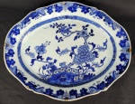 COMPANHIA DAS INDIAS  EX COLEÇÃO CONDE GUILHERME PRATES  GRANDE  TRAVESSA EM PORCELANA CHINESA DITA COMPANHIA DAS INDIAS REINADO QIANLONG (1735 -1796). DECORAÇÃO EM AZUL UNDERGLAZE COM PEÔNIAS, CERCAS E LUXURIANTES RAMAGENS REALÇADAS A OURO.  A BASE TEM A DESEJÁVEL FINALIZAÇÃO UNGLAZED (SEM COBERTURA DO ESMALTE) QUE MOSTRA A PASTA RUGOSA DA PORCELANA COM A COR NATURAL DA ARGILA (TÍPICA DA BOA PRODUÇÃO DO PERÍODO QIANLONG). PERTENCEU A COLEÇÃO DO CONDE GUILHERME PRATES. CHINA, MEADOS DO SEC. XVIII. 43 CM DE COMPRIMENTO