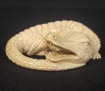 IMPRESSIONANTE NETZUKE  ESCULPIDO EM MARFIM. COM GRANDE REALISMO  ESSA LINDA ESCULTURA REPRESENTA FIGURA DE CROCODILO EM PRIMORASA ESCULTURA. ASSINADO SOB A BASE. CHAMA A ATENÇÃO ALÉM DO EXCELENTE TRABALHO O TAMANHO AVANTAJADO DO NETZUKE. JAPÃO, SEC. XIX. 8 CM DE COMPRIMENTO.NOTA: Os netzukes são na verdade botões que surgiram no Japão para atender uma necessidade prática. Os quimonos tradicionais utilizados pelos homens não possuíam bolsos entretanto os seus usuários necessitavam de lugar para guardar seus pertences pessoais (tubos, tabaco, dinheiro, selos, medicamentos). A solução foi colocar tais objetos em recipientes denominados Sagemono pendurados por faixas nos quimonos. O fixador desses recipientes na vestimenta era uma pequena escultura que funcionava como botão chamada Netzuke. Do Japão propagou-se para a China. Com o tempo os netzukes foram evoluindo para objetos de grande mérito artístico e expressão, um símbolo de habilidade extraordinária. Eles tem uma longa história na refletindo aspecto da cultura chinesa e japonesa, quer seja do folclore ou da vida cotidiana. Então ao se deparar com uma pequena escultura com dois pequenos orifícios perpendiculares sob a base saiba que esta diante de um Netzuke.