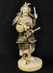 IMPRESSIONANTE OKIMONO EM MARFIM COM FEITIO DE SAMURAI PORTANDO ARMADURA, SUAS ARMAS E UM LEQUE. ASSINADO SOB A BASE. JAPÃO FINAL DO SEC. XIX. 18 CM DE ALTURA