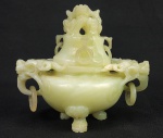 FORMIDÁVEL INCENSÁRIO ENTALHADO EM JADE. TAMPA COM TOPO APRESENTANDO FIGURA DE DRAGÃO SENTADO SEGURANDO OS PRÓPRIOS JOELHOS COM AS MÃOS E DOTADA DE TRÊS  ARGOLAS  LATERAIS. ALÇAS COM FEITIO DE ELABORADAS CABEÇAS DE DRAGÕES MORDENTES DE ARGOLAS. GRANDEQUALIDADE DE EXECUÇÃO! TRABALHO ERUDITO! CHINA, PERIODO MINGUO, 16 CM DE DIAMETRONOTA: Ao longo da história chinesa, os materiais mais valorizados foram jade, bronze, seda e laca. O jade é considerado altamente valioso e tem sido estimado há milhares de anos. Objetos de jade de animais e réplicas de ferramentas e armas foram descobertos em antigas tumbas chinesas, que datam de 7.000 anos. Por causa de sua raridade e dureza, na China antiga era um material freqüentemente usado para cerimônias, adornos e rituais. A palavra chinesa para Jade é yu, que na verdade tem um significado mais geral para incluir muitos tons de pedras duras verdes, cinzas e marrons. Jade se refere a dois tipos de minerais, jadeíte e nefrita. O jade é feito de alumínio e um silicato de sódio. A jadeita, que foi encontrada na Birmânia, é de um verde mais escuro e não era usada na China até o século XVIII. A nefrita, encontrada na China central, é mais clara e também apresenta variações de cores. Ambos são bastante fortes e difíceis de trabalhar devido à sua estrutura cristalina compacta. Os objetos de jade encontrados na China antes do século 18 são, na verdade, nefrita. Jade foi encontrado em rios onde pedras quebraram e caíram. Os artesãos então os cortam em fatias para começar seu trabalho. Para trabalhar em formas esculturais, eles devem ser polidos com areia abrasiva. Os chineses produziram um número surpreendentemente grande de belas esculturas de jade, considerando como o material é difícil de trabalhar. É polido com um acabamento muito suave e a textura e aparência do material tem referência simbólica à pureza, beleza, imortalidade e sabedoria.