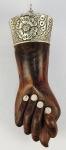 JÓIA DE CRIOULA - GRANDE FIGA EM JACARANDÁ COM ADEREÇOS EM PRATA DE LEI BAHIA, SEC. XIX. 28 CM DE COMPRIMENTO. NOTA: No Brasil, esse sinal simboliza os desejos de boa sorte. Muito comum na cultura dos escravos africanos era usado como amuleto contra olho gordo na crença de que o obsceno distraia o mal. Este exemplar em pregão é obra de primorosa qualidade denotando tratar-se de trabalho de artífice elevado nível técnico. A figa originalmente um amuleto italiano, chamado Mano Fico, também era usada pelos etruscos na era romana. Mano significa mão e Fico ou Figa é a representação dos genitais femininos, e era associado a fertilidade e erotismo. Na Itália este sinal, conhecido como "fica" ou "far le fiche", pela semelhança com a genitália feminina, foi um gesto comum e muito grosseiro em séculos passados assim como na Turquia