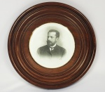 CONDE EDUARDO DA SILVA PRATES - RETRATO DO CONDE PRATES TRANSFERIDO PARA PLACA EM PORCELANA. MOLDURA CIRCULAR EM MADEIRA, ÓCULO EM VIDRO BIZOTADO. BRASIL, SEC. XIX. 34 CM DE DIAMETRO.NOTA: EDUARDO DA SILVA PRATES (1860-1928), o CONDE DE PRATES, Filho de FIDÊNCIO NEPOMUCENO PRATES e de DONA INOCÊNCIA DA SILVA PRATES (sendo esta filha do BARÃO DE ANTONINA, JOÃO DA SILVA MACHADO).  Seu pai era médico formado pela Faculdade de Medicina do Rio de Janeiro, tendo sido Deputado por duas vezes pela Assembléia Geral na Legislatura do Império. O fato do progenitor ser um político bem sucedido, não motivou Eduardo Prates a seguir nessa direção como seria natural. Sua vida foi dedicada ao empreendedorismo e a uma trajetória de sucesso como poucas na história do Brasil.  Veio a se casar em 1886, com ANTONIA DOS SANTOS SILVA, de velha estirpe paulista, filha do BARÃO DE ITAPETININGA e da BARONESA DE TATUÍ, proprietários das terras que propiciaram a primeira expansão do núcleo histórico paulistano, em direção à hoje Praça da República. Com o casamento tornou-se concunhado do Marquês de Três Rios, uma das maiores fortunas do Império. A morte dos Marqueses de Três Rios, sem geração havida de seu matrimônio, fez com que a Fazenda Santa Gertrudes,  herança de DONA MARIA HYPÓLITA DOS SANTOS, fosse destinada à  sua meia irmã DONA ANTÔNIA DOS SANTOS SILVA (filha do segundo casamento do BARÃO DE ITAPETININGA com DONA CORINA DE SOUZA CASTRO, viúva do BARÃO DE TATUÍ). EDUARDO PRATES não era afeito aos negócios de Fazendas. Sua fortuna era baseada nos ramos imobiliário, bancário e Férreo. Entretanto mais do que um agricultor era um visionário homem de negócios que levou a Fazenda Santa Gertrudes a um patamar de grandeza talvez nunca sonhado por seus proprietários anteriores. Apesar das alterações resultantes da mudança de proprietário em 1895 não houve quebra no ritmo ascendente da fazenda acelerando, ainda mais, seu crescimento. Tornou-se proprietário da fazenda num período excepcionalmente favorável à expansão do café. Eduardo Prates era ativo homem de negócios, o capitalista de São Paulo, e, em 1895 se viu fazendeiro de café, proprietário da Fazenda Santa Gertrudes, considerada uma das mais importantes cafeeiras no estado. Não era Eduardo Prates para FAZENDA SANTA GERTRUDES o pioneiro em terras novas a despender energia e capacidade na luta contra a natureza como foram seus antecessores no domínio dessas terras, mas foi um proprietário enérgico e capaz, preocupado em estabelecer uma tecnologia mais avançada para o maior desenvolvimento de sua propriedade. Era o citadino transformado em fazendeiro, que ao receber como herança à fazenda, levou para o campo toda a sua vivência de homem de negócios, sempre aberto às inovações e desta maneira agigantou o legado ao ponto da propriedade acabar por gerar o núcleo urbano da futura cidade paulista de Santa Gertrudes. Na área de negócios, o Conde era conhecido por seu espírito empreendedor e sempre demonstrou talento: foi fundador e presidente do Banco de São Paulo dedicou-se ativamente as atividades comerciais (importações e imóveis urbanos), fomentou a Companhia Paulista de Estradas de Ferro (sendo diretor desta), criou a  Companhia de Armazéns Gerais de São Paulo (na qual atuou como presidente) e ainda a outras companhias de transportes e indústrias, como a Companhia Paulista de Navegação e a Companhia Frigorífica e Pastoril de Barretos (vice-presidente). Contribuiu com a municipalidade de São Paulo ao colaborar com o Plano Bulevar, modificando o ambiente e melhorando as edificações da Rua Líbero Badaró, sendo que sua maior contribuição foi nas negociações para que o solar dos Barões de Itapetininga (uma imensa chácara), existente nesta rua, fosse doada para o município e assim transformar-se no Parque do Anhangabaú. Prates também foi presidente, em 1896, da Associação Comercial de São Paulo (ACSP), sucedendo ao Coronel Rodovalho e iniciando a luta contra o projeto de pagamento em ouro dos direitos aduaneiros, além de ter sido um dos fundadores do Automóvel Clube de São Paulo, e da Sociedade Rural Brasileira.