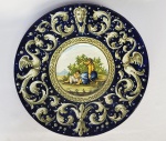 TRADIÇÃO DE DERUTA - LINDO MEDALHÃO EM MAIOLICA COM RICA DECORAÇÃO EM ESMALTE AO GOSTO RENASCENTISTA. FORMA PAR COM O ANTERIOR.  POSSUI ANTIGA ETIQUETA DO BAZAR PARISIEN NA RUA DE SÃO BENTO EM SÃO PAULO (VIDE NOS CRÉDITOS EXTRAS DESSE LOTE PROPAGANDA DO BAZAR PARISIEN NA DEC. DE 1910). ITÁLIA, SEC. XIX/XX.  37 CM DE DIAMETRO. NOTA: Originalmente, maiolica ou di maiolica referia-se à cerâmica esmaltada e pintada semelhante à dosmouros da Espanha muçulmana que costumava chegar à Itália através de Maiorca. Foi decorado com motivos orientais, e ficouainda mais rico por um tipo particular de verniz iridescente que mudou do vermelho rubi ao amarelo isabelino e ao verde voador espanhol, das nuances frias e prateadas do metal aostons mais quentes do ouro. Esta decoração foi reproduzida de forma flagrante pelos nossos oleiros e foi feita sobre peças já envernizadas e assadas, que depois foram assadas mais uma vez num forno reverberatório especial . A versão italiana da cerâmica mourisca era também conhecida como di maiolica oumaiolica, mesmo sem a iridescência característica dada pelo terceiro processo de cozimento, que era particularmente comum nos ateliês de Deruta e Gubbio, onde o mestre Giorgio Andreolitrabalharia peças já pintadas. A verdadeira invenção da maiolica italiana foi o uso habilidoso de uma paleta pictórica completa em sua superfície estanífera empoeirada antes da segunda cozedura, logo após o envernizamento do medalhão. É uma mistura de mil ideias e expedientes experientes capazes de criar algo novo, uma evolução que atingiu o seu ápice no início dos anos 500. São invenções absolutas e inimitáveis, segredos que cada ateliê considerou seus, símbolos de um nível de respeitabilidade quase sempre sinônimo de sucesso.