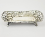 ESPIVITADEIRA E BERÇO EM PRATA DE LEI COM MARCAS PARA O RIO DE JANEIRO (COROA SOB FI) MOITINHO PAG.; 370. DECORADA COM FLORES E RAMAGENS E ANANASES. ASSENTE SOBRE QUATRO PÉS EM GARRA. BRASIL, CIRCA DE 1830. 20 CM DE COMPRIMENTO. 485 G