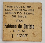RELICARIO DE FREI FABIANO DE CRISTO   RELIQUIA DE SEDA QUE TOCOU OS OSSOS DE FREI FABIANO DE CRISTO EM MARIANA, MG. FREI FABIANO DE CRISTO É OBJETO DE DEVOÇÃO POR SUA VIDA DEDICADA A DEUS E AOS HOMENS NO BRASIL COLONIAL FALECEU EM 1747. 3 X 3 CMNOTA: Ao norte de Portugal, numa aldeia chamada Soengas, nasceu a 8 de fevereiro de 1676, Frei Fabiano de Cristo, que no século se chamava João Barbosa. Filho de Gervásio Barbosa e da Senhorinha Gonçalves, formavam uma das muitas famílias de vida simples que ali viviam, dedicadas sobretudo ao cultivo da uva.De suas cinco irmãs, quatro se fizeram religiosas, o mesmo acontecendo com o único filho da família. Pouco se sabe sobre os anos de infância e adolescência de João. Sabe-se apenas que pela vida simples e pobre que levavam, pouca oportunidade teve de travar contato com os livros.À procura de algo mais  João Barbosa sabia que o ambiente que o cercava não era resposta aos seus ideais. Sabia que sua família fora, outrora, abastada e que em suas veias corria a nobreza antiga, agora oculta na pobreza. Por ser ambicioso, sentiu logo o desejo de restabelecer a antiga nobreza. Mas não seria em Soengas que isso poderia acontecer. No primeiro instante pareceu-lhe que o melhor caminho seria o comércio. Dirigiu-se então à cidade do Porto, onde as possibilidades se mostravam mais abundantes e ricas. Aí ouvia histórias fantásticas de terras distantes e muita riqueza, deixando o jovem João muito entusiasmado. No final do século XVII, a novidade mais ambiciosa que os marinheiros traziam a Portugal era a descoberta abundante do ouro em Minas Gerais. Assim como muitos, também João viu lá longe, no Brasil, despontar a solução de seus problemas.João despede-se de seus pais e irmãs e parte para o Brasil numa penosa viagem de meses de balanço no mar e outra não menos penosa por terra, até chegar ao seu destino, na região das promessas douradas: o Ribeirão de Nossa Senhora do Carmo (hoje Mariana) e Ouro Preto. Muita riqueza foi vista, muitos homens arrancavam da terra quantidades enormes de ouro que os tornavam ricos da noite para o dia. Mas, paralelamente à exploração das minas, surge outra fonte de renda: a vida do comércio ou carreira das minas. Foi esta a profissão que João escolheu logo que chegou ao Brasil.Não sabemos exatamente qual a especialidade dos negócios de João. Sabemos apenas que em pouco tempo conseguiu uma respeitável fortuna. A partir de 1704, vamos encontrar João Barbosa com residência fixa na vila de Parati, tocando seus negócios que lhe rendiam bons lucros, mas nunca deixando de manter contato com as coisas de Deus. Assim ligou-se logo ao pároco da vila, auxiliando-o em tudo. Todas as obras de caridade recebiam dele largas quantias em dinheiro, não deixando nunca de ajudar os pobres, que encontravam nele a mão generosa sempre pronta a ajudar.Os planos de João eram de trabalhar mais alguns anos e regressar a Portugal com suficiente fortuna para alterar a situação de sua família. Mas aí Deus entrou em sua vida de forma diferente e alterou o plano do homem. O trabalho espiritual exercido em Parati foi mudando as concepções de João. Foi sentindo cada vez mais forte o convite à vida religiosa. Hesita. Esperava maior clareza. Algum sinal, talvez. Mas um acontecimento trágico veio pôr fim às suas hesitações. A morte por assassinato de um sócio e companheiro seu, por motivos desconhecidos, fez com que João ficasse profundamente abalado e percebesse como os bens materiais não significam nada diante da grandeza de Deus.Nesta altura da história, muitas Ordens Religiosas já estavam estabelecidas no Brasil. Examinando-as, pode sentir que nenhuma estava tão de acordo com seus propósitos como a Ordem Seráfica de São Francisco de Assis. Porque, como nascera na pobreza, passara depois à riqueza pelo trabalho, queria à luz da fé voltar a ser pobre. E ninguém melhor que Francisco de Assis para guia nesta troca de valores.O Franciscano  Tomada a decisão, João apresentou-se ao Padre Provincial, no Convento Santo Antônio do Rio, que percebeu imediatamente suas qualidades e, sobretudo, um homem que sentia o chamado de Deus, logo sendo admitido à vida franciscana. Primeiro passo de João: desfazer-se de todos os bens. Dividiu toda a sua fortuna em três partes: a primeira foi enviada a Portugal para a família e para outros acertos; a segunda parte foi destinada às obras de caridade; e a terceira foi distribuída entre os pobres. Assim, a 8 de novembro de 1704, apresentou-se no Convento São Bernardino em Angra dos Reis, e no dia 11 de novembro trocou suas vestes seculares pelo hábito marrom de São Francisco, trocando também seu nome de João para Frei Fabiano de Cristo, nome pelo qual é conhecido ainda em nossos dias, pois foi a partir desta troca que ele enveredou pelos caminhos da santidade.Frei Fabiano de Cristo, no tempo de formação, optou por ser irmão franciscano.No Convento Santo Antônio do Rio  No final do ano de 1705, Frei Fabiano de Cristo recebeu ordens de transferir-se para o Convento Santo Antônio do Rio de Janeiro, com o encargo de porteiro. Aliás, na Ordem Franciscana dava-se particular importância a esta função, pois prescrevia-se fosse ela entregue somente a religiosos de muita prudência, confiança e virtude, após 15 anos de hábito. A nomeação de Frei Fabiano de Cristo era um reconhecimento à sua virtude e confiança, pois estava apenas há dois anos na Ordem. Apesar do bom trabalho exercido por Frei Fabiano na portaria, os superiores pediram, no ano de 1707 ou 1708, que ele tomasse conta da enfermaria. Imediatamente obedeceu e, aqui como na portaria, deu belíssimo exemplo de caridade.Embora não tivesse preparação especial para esta função, a caridade e o esforço pessoal substituíam as deficiências. Praticamente levava sua vida junto aos doentes, a tal ponto que nem sequer tinha um quarto próprio, por longo tempo, contentando-se em dormir em qualquer lugar da enfermaria, para que, dia e noite, pudesse estar à disposição dos doentes. Só mais tarde aceitou um quarto, mas sempre junto à enfermaria. Assim consumiu quase todo o resto de sua vida, cerca de trinta e oito anos, exercendo sua caridade para com os doentes e idosos.Enfermidade e morte  Com o passar do tempo, o corpo de Frei Fabiano foi sentindo o peso da idade e dos sacrifícios, na forma de sofrimento físico que o crucificaram por quase 30 anos. A causa inicial destes sofrimentos foi uma erisipela crônica, localizada nas pernas, acentuadamente na esquerda, que mais tarde se transformou numa horrível chaga. Para aumentar estes sofrimentos nas pernas, apareceu-lhe um quisto num dos joelhos, atribuído por alguns ao tempo excessivo que o bom irmão permanecia de joelhos nas suas longas horas de oração.Jamais se ouviu dele a mínima queixa ou atitude de revolta diante de tanto sofrimento. A única coisa que o atormentava era o fato de não poder mais exercer sua função de enfermeiro. Seu estado de saúde agravou-se muito, já estava ele na casa dos 70 anos. Pressentiu que ia chegando ao fim de seus dias e, conforme dizem, chegou a anunciar aos confrades o dia e a hora de sua morte.No dia 17 de outubro de 1747, pelas 14h00, Frei Fabiano de Cristo, rodeado pelos confrades, quase despercebidamente como vivera, parte ao encontro do Pai.Uma multidão tomou conta do Convento Santo Antônio. Todos queriam se despedir de Frei Fabiano, pois ele era visto como um Santo, um Servo de Deus. Todos desejavam ver e tocar aqueles restos que representavam a santidade.O local onde estavam encerrados os ossos de Frei Fabiano começou a ser abandonado, terminando por cair em ruínas. Dos cento e tantos religiosos do tempo de Frei Fabiano o Convento não abrigava, em 1870, mais que seis e, aos poucos, o Convento foi se transformando numa espécie de hospedaria até que, em 1885, Dom Pedro II hospedou ali o sétimo Batalhão de Infantaria do Exército. E vieram as depredações e os estragos. A ruína começara um trabalho demolidor, levando consigo a placa de bronze que assinalava o local da urna com os ossos de Frei Fabiano. Assim, quando o batalhão se retirou, ninguém mais sabia o local que se encontrava a urna. Inclusive acreditava-se que a mesma havia sido violada.O reencontro  Não queria Deus fosse este o fim dos ossos de Frei Fabiano, pois em fins de janeiro do ano de 1924, chuvas fortes e prolongadas, causaram grandes estragos no Rio e em vários Estados. Às três horas da madrugada do dia 2 de fevereiro, com um estrondo terrível, ruiu grande parte do muro, atrás do qual, antigamente, se achava a enfermaria. Em meados de abril, foram iniciadas as obras de reconstrução do dito muro, derrubando a 1 de maio do ano de 1924, o resto do muro que ainda não ruíra. Parte do muro já havia sido derrubado, quando do lado do Convento, de repente, apareceu uma urna de chumbo, cheia de ossos. Imediatamente entregue ao Guardião, este logo ficou convencido de tratar-se dos ossos de Frei Fabiano. Abrindo a urna, encontrou em cima, coberto de cal, um documento em péssimo estado, onde ainda se lia: Frei Fabiano.. enfermeiro deste convento.. Rio...Resolveram então encerrá-los em uma urna de mármore, com uma pequena abertura lateral, por onde se poderiam ver os ossos. A urna foi colocada numa capela, do lado esquerdo da Igreja do Convento Santo Antônio. E a veneração recomeçou. Em pouco tempo, os fiéis começaram a procurar o santo irmão, como nos primeiros dias após sua morte. Ainda hoje, a procissão de devotos continua a desfilar diante do altar singelo que abriga os ossos de Frei Fabiano. De todos os cantos do Brasil chegam cartas comunicando graças e pedindo lembranças do santo irmão que, pequeno na terra, continua no céu uma presença benéfica, atestando como Deus é magnífico em seus santos, pois neles manifesta sua imensa misericórdia e sua paterna solicitude de ajudar os homens pelos homens.