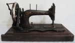DIVERSOS, Máquina de costura a manivela, marca SINGER, confeccionado em ferro esmaltado na cor preta, com flores e folhagens e realces em dourado, apresenta oxidação. Base retangular em madeira. Manivela travada (faltando cabo), Med: 23x35x15cm. Acompanha capa em madeira.