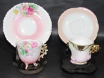 PORCELANA, Duas xícaras de coleção com seus respectivos pires em porcelana esmaltada, sendo: A) 1 na tonalidade branca, decorado com flores e folhagens em policromia, pintura degradê rosa e branca, apoiado sobre três pés, filetada a ouro com falhas na douração (6x7,5x6cm) e B) 1 em porcelana alemã na tonalidade branca, decorado em policromia e realces em ouro, pega no feitio de flor com vasta douração, apresenta 1 fio de cabelo (5,5x7,5x6cm).