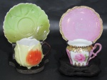 PORCELANA, Duas xícaras de coleção com seus respectivos pires em porcelana esmaltada, sendo A) 1 no feitio de fruto com pintura policromada, apresenta 1 bicado na borda, pires com 1 fio de cabelo (5,5x7x5cm) e B) 1 na tonalidade rosa, com pintura de flores e folhagens em policromia, realces em dourado, borda perolada, 1 discreto bicado (4,5x7,5x4,5cm).