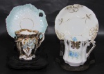 PORCELANA, Duas xícaras de coleção com seus respectivos pires em porcelana esmaltada na tonalidade branca, sendo A) 1 com vasta douração decorada com flores em relevo na tonalidade azul, apresenta falhas na douração (5,5x6x5cm) e B) 1 na tonalidade branca, com pintura de flores e folhagens em policromia e realces em dourado, pires apresenta fio de cabelo (5,5x6,5x5cm).