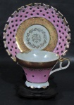 ROYAL HALSEY, Xícara de coleção com seu respectivo pires em porcelana esmaltada na tonalidade rosa, borda com faixa dourada decorada com motivos vegetalistas em vermelho, guirlanda floral em dourado, interior furtacor, pires decorado com vazados. Med.: 6,5x11,5x9cm.