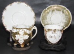 PORCELANA, Duas xícaras de coleção com seus respectivos pires em porcelana esmaltada, sendo A) 1 decorado com coração terminado em volutas em relevo em vasta douração, com inscrição AMIZADE em dourado, apresenta falhas na douração (5,5x7,5x6cm) e B) 1 decorado com flores e folhagens em relevo, apoiado sobre 4 pés, corpo gomado em vasta douração com falhas na douração, pires adaptado (6x8x6,5cm).