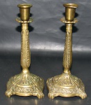 ARTE SACRA, Par de castiçais em bronze, apoiado sobre 4 pés, ricamente cinzelado por elementos vegetalistas, bobeche no feitio de flor (possui mossas). Med.: 20,5cm.