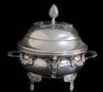 METAL PRATEADO, Sopeira em metal espessurado a prata, ricamente decorada por florões, laçarotes e querubins em relevo, tampa com guirlanda floral e pega no feitio de pinha, apoiada sobre 4 pés. Marcado S. RITA . Tampa com pequenas mossas. Banho novo. Med.: 30x33x26cm.