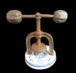 PORCELANA, Quebra nozes em ferro fundido, apoiado sobre base em porcelana esmaltada na tonalidade branca com pintura de motivos florais na tonalidade azul, pega representando noz, possui sinais de oxidação. Med.: 9x7cm.