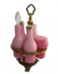 THOMAS WEBB, Galheteiro com 5 peças em vidro acetinado dito (satinglass) na tonalidade rosa com interior leitoso, sendo: A) 2 galhetas (azeite e vinagre), 1 com tampa em vidro adaptada (bicados), e uma sem tampa com bicados na borda (15cm), B) 1 saleiro e paliteiro com tampa em metal dourado (16cm), C) 1 porta mostarda sem tampa (10x5,5cm), e D) 1 suporte em bronze, ricamente cinzelado por elementos vegetalistas, apoiado sobre base circular tripoide (28,5cm).