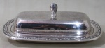 ONEIDA, Manteigueira em metal espessurado a prata, borda e pega da tampa cinzelada por elementos vegetalistas, recipiente em vidro translucido. Med.: 7x20x12cm.
