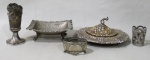 METAL PRATEADO, Lote com 5 peças, sendo: A) 1 manteigueira em metal espessurado a prata, ricamente cinzelado por elementos vegetalistas (falta o recipiente em vidro e necessita banho) (16x7,5cm), B) 1 saboneteira em metal espessurado a prata com decoração martelada e elementos geométricos, marcado no fundo BOLIVIA (4,5x13x11cm), C) 2 floreiras em metal espessurado a prata de decorações distintas (necessitam banho) (11cm / 5cm) e D) 1 porta alianças em metal espessurado a prata cinzelado por elementos vegetalistas (falta recipiente em vidro) (3x6x4cm).