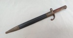 MILITARIA, uma (1) antiga baioneta em aço (cutelaria militar), século XIX/XX, usada no rifle Mauser, sem marca de manufatura aparente, possivelmente alemã, com cabo em madeira, pomo e guarda mão em metal, bainha em couro com ponteira em metal, usada, sinais de oxidação,medindo 45 cm comprimento.