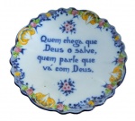 FAIANÇA, Alcobaça, Portugal, Medalhão confeccionado em faiança vitrificada, com pintura de flores, folhagens e concheados em policromia com inscrição no centro: QUEM CHEGA QUE DEUS O SALVE, QUEM PARTE QUE VÁ COM DEUS. Marcado no verso. Med.: 30,5cm.