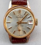 RELÓGIO, um (1) de pulso da marca MONDAINE (Mondaine Watch Ltd., relojoaria fundada em 1944, por Hans Hilfiker, em Zurique, Suíça), mostrador prateado, possui calendário, caixa em metal dourado, pulseira em couro, medindo 20 mm diâmetro, mecânico, mecanismo a corda com 17 rubis ou safiras, parado, usado, não testado e sem garantia.