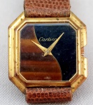 RELÓGIO, um (1) de pulso, da GRIFE CARTIER (fundada em 1845 em Paris, por Louis-François Cartier, fabricante de Jóias, Relógios e objetos de luxo; tornada célebre pelo seu filho Louis Cartier; esteve sobre o comando da família até o ano de 1964; atualmente pertence a Compagnie Financière Richemont S/A), Suíço, caixa espessada a ouro 18k por eletrólise plaqué dor, medindo 27 x 27 mm, pulseira em couro com bastante sinais de gasto, movimento mecânico funcionando, mecanismo com 17 rubis ou safiras, usado e sem garantias.