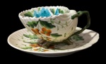 PATENT, Xícara de coleção para chá com seu respectivo pires em porcelana esmaltada na tonalidade creme no feitio de concha, pintura floral em rica policromia, pés e alças no feitios galhos e borda filetada a ouro, apresenta falhas na douração. Med.: 6x12,5x10cm / 16,5x16cm.