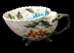 PATENT, Xícara de coleção para chá em porcelana esmaltada na tonalidade creme no feitio de concha, pintura floral em rica policromia, pés e alças no feitios galhos e borda filetada a ouro, apresenta falhas na douração. Apresenta 1 bicado e fio de cabelo Med.: 6x12,5x10cm.