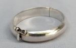 JOIA, um (1) bracelete rígido, meia cana, modelo dito escrava, confeccionado em PRATA, liso, possui pega ladrão, medindo 7 x 6 cm, largura 1,1 cm, peso aproximado 26 gr.