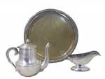 METAL PRATEADO, Lote com 3 peças em metal espessurado a prata, sendo: A) 1 prato redondo com rico cinzelado de elementos vegetalistas, necessita banho (32cm), B) 1 bule para chá , corpo liso, pega da tampa no feitio de pinha, necessita banho (17x21x8,5cm) e C) 1 molheira com cinzelado perolado e corpo liso (9,5x20x9cm).