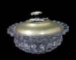 VIDROS, Bomboniere em vidro translucido ricamente lapidada em relevo, bordas onduladas, tampa em metal espessurado a prata com pega da tampa no feitio de flores e folhagens. Med.: 9x15cm.