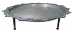 METAL PRATEADO, Grande bandeja redonda de pé em metal espessurado a prata, ricamente cinzelada por motivos florais, galeria vazada, borda em relevo decorado por arabescos e concheados, apoiado por 3 pés de rosca. Necessita banho. Med.: 16x52cm.