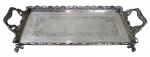 METAL PRATEADO, Bandeja retangular em metal espessurado a prata, fundo cinzelado por frisos, galeria ricamente decorada por flores, folhagens e concheados com vazados, apoiado sobre 4 pés em garra. Med.: 8x40x16cm.