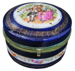 PORCELANA, Caixa porta joias redonda, confeccionada em porcelana esmaltada na tonalidade azul, com pintura de cena galante, flores e folhagens em policromia e florões realçados em ouro, guarnições em metal dourado com cinzelado perolado. Med.: 9x15cm.