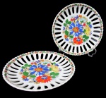 SCHMIDT, Par pratos decorativos em porcelana esmaltada na tonalidade branca, com pintura de flores e folhagens em rica policromia, galeria vazada e borda com guirlanda floral. Med.: 19,5cm.
