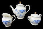 NORITAKE, Parte de serviço para chá, confeccionadas em porcelana esmaltada na tonalidade branca, arabescos realçados em relevo, pintura de flores e folhagens na tonalidade azul e bordas filetadas a ouro, sendo: A) 1 bule para chá (17x21x8,5cm), B) 1 açucareiro (10x13x7cm) e C) 1 leiteira (10x10x5,5cm).
