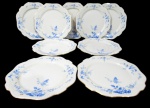 NORITAKE, Dez pratos rasos, confeccionadas em porcelana esmaltada na tonalidade branca, arabescos realçados em relevo, pintura de flores e folhagens na tonalidade azul e borda filetadas a ouro. 1 com falhas na douração Med.: 21,5cm