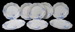 NORITAKE, Oito pratos rasos, confeccionadas em porcelana esmaltada na tonalidade branca, arabescos realçados em relevo, pintura de flores e folhagens na tonalidade azul e borda filetadas a ouro. 2 com falhas na douração Med.: 23cm.