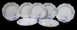 NORITAKE, Sete pratos rasos, confeccionadas em porcelana esmaltada na tonalidade branca, arabescos realçados em relevo, pintura de flores e folhagens na tonalidade azul e borda filetadas a ouro. 2 com falhas na douração Med.: 23cm.