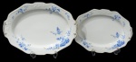 NORITAKE, Duas travessas ovais, confeccionadas em porcelana esmaltada na tonalidade branca, arabescos realçados em relevo, pintura de flores e folhagens na tonalidade azul e borda filetadas a ouro. Med.: 36x26cm / 31x22cm.