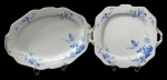 NORITAKE, Prato para bolo e travessa oval, confeccionadas em porcelana esmaltada na tonalidade branca, arabescos realçados em relevo, pintura de flores e folhagens na tonalidade azul e borda filetadas a ouro. Med.: Prato para bolo: 30,5x27,5cm / Travessa: 36x26cm.