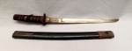 CUTELARIA, um (1) KATANA OMIAGUE, lâmina sem gume, com sinais de oxidação; TSUBA em ferro com singelo relevo em elementos vegetalistas; empunhadura em tresse de tecido e outros materiais; bainha em madeira laqueada com ponteira em metal cinzelado em elementos vegetalistas, medindo 59,5 cm comprimento, vide foto.