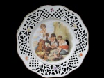 BAVARIA, Alemanha, Prato decorativo em porcelana esmaltada na tonalidade branca, centro com pintura de crianças em policromia, borda decorada com vazados, flores e folhagens em policromia, filetada a ouro, marcado no verso. Med.: 29cm.