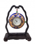 LION DO, Relógio de mesa, confeccionado em metal dourado, esmaltado na tonalidade azul, com pintura de dragões chineses em cloisone, funcionamento a bateria, suporte em madeira apoiado sobre base retangular. Não testado e sem garantia de funcionamento. Med.: 19x15x6cm.