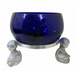 VIDROS, Saladeira confeccionada em vidro na tonalidade azul, formato bojudo, apoiado sobre base em alumínio polido, sustentado por 3 querubins. Med.: 30x29cm. Possui 2 discretos bicados na borda.