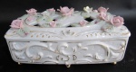 PORCELANA, Caixa porta joias em porcelana esmaltada na tonalidade branca, decorado com arabescos, flores e folhagens em relevo e policromia, tampa com vazados, realces em ouro, com falhas na douração. Med.: 10x20x11,5cm. Possui algumas flores bicadas.
