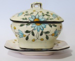 FAIANÇA, Pequena molheira c/ presentoir, confeccionada em faiança vitrificada na cor creme, com pintura de flores e folhagens em policromia. Med.: 8x9x7cm / 11,5x9cm. Apresenta craquele na tampa.