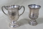 METAL PRATEADO - Dois troféus em metal espessurado a prata de modelos, decorações e comemorações distintas. 1 apresenta mossas. Med.: 10x11x6,5cm / 10x6cm.