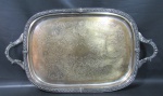 METAL PRATEADO - Grande bandeja em metal espessurado à prata inglês, bordas com decoração torneada e frisada, alças com detalhes de folhagens, centro cinzelado com flores, folhagens, acantos e volutas. Necessita banho de prata. Medidas 4 x 64 x 38 cm