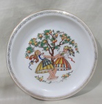 CHODZIEZ, Polônia, Medalhão em porcelana polaca esmaltada na tonalidade branca com pintura de camponesas e macieira em policromia, borda com guirlanda floral em ouro. Falhas na douração. Med.: 31cm.
